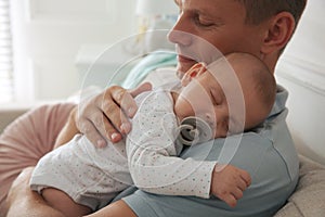 Happy father holding his cute sleeping baby with pacifier at home