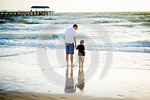 Happy father holding holding hand of little son walking together on the beach with barefoot