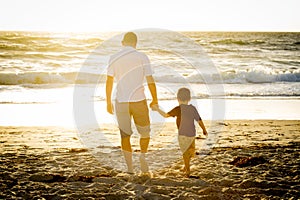 Happy father holding holding hand of little son walking together on the beach with barefoot