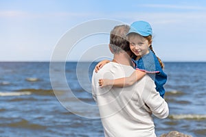 Happy father hugging his little daughter on the beach, father and daughter walking on the beach and posing to camera