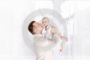 Happy father kisses newborn baby at home by the window, happy loving family concept, father`s day