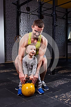 Happy father and little cute son exercising with dumbbells and smiling while against brick wall.