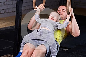 Happy father and little cute son exercising with rings and smiling.