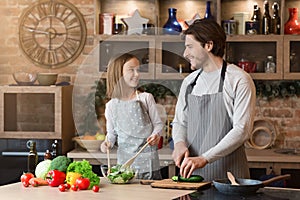 Happy father and little daughter cooking healthy salad in kitchen, cutting vegetables