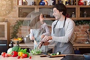 Happy father and little daughter cooking vegetable salad in kitchen