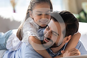 Happy father and little daughter hugging, lying on couch together