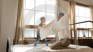 Happy father and little daughter playing pillow fight on bed