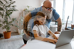 Happy father with little girl do hometask on contemporary laptop at table in room photo