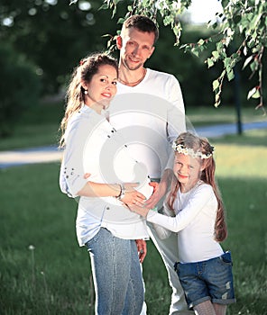 Happy father and little girl hugging her pregnant mother on a wa