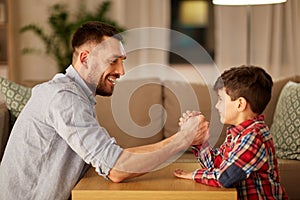 Happy father and little son arm wrestling at home