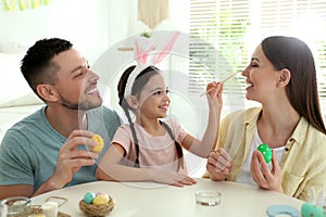 Happy father, mother and daughter having fun while painting Easter eggs at table