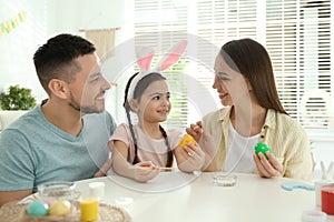 Happy father, mother and daughter painting Easter eggs at table