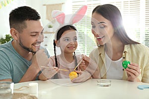 Happy father, mother and daughter painting Easter eggs at table