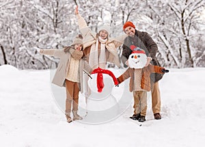 Happy father, mother and kids having fun outdoor while making snowman together in winter snowy park