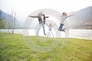 Happy father, mother and little girl jumping near lake on a beautiful sunny day