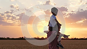 A happy father plays with his son while running through a wheat field. A small boy sits on his father`s shoulders