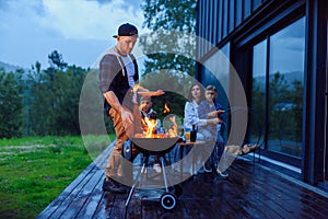 Happy father preparing a barbecue on a family vacation on the terrace of their modern house in the evening.