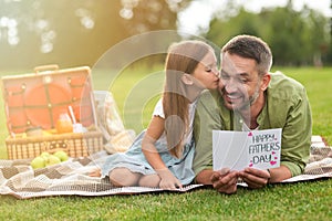Happy father received handmade postcard from his daughter, little girl and her daddy having a picnic in the park on a