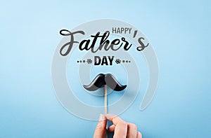 Happy Father`s Day background concept with hand holding black mustache on bright blue blackground