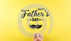 Happy Father`s Day background concept with hand holding black mustache with the text on pastel yellow background