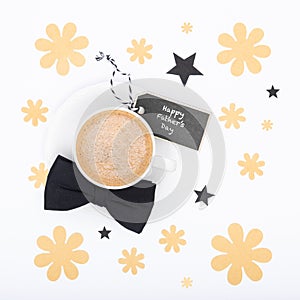 Happy Father`s Day Background. Cup of coffee and black bow tie on white background flat lay. Floral Fathers day.