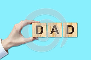 Happy father`s day background. Female hand with the word, dad written on wooden blocks. Blue background Congratulatory background