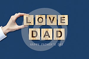 Happy father`s day background. Female hand with the word, Love dad written on wooden blocks. Dark background Congratulatory