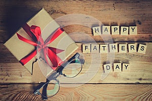 Happy father`s day block and gift box with glasses on wood backg