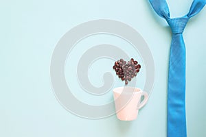 Happy Father`s Day concept with blue colour necktie and coffee cup with coffee beans heart shape on pastel