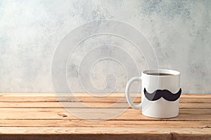 Happy Father`s day concept with coffee mug and mustache over wooden background