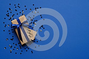 Happy Father`s day concept. Gift box with blue ribbon bow and confetti on blue background top view. Fathers day greeting card