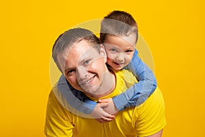 Happy father`s day! Emotional father and son hugging on yellow background