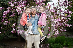 Happy Father\'s Day. Father with two daughters in hands enjoying nice spring day near magnolia blooming tree