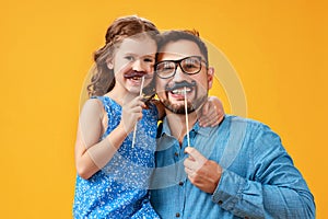 Happy father`s day! funny dad and daughter with mustache fooling around on yellow background