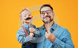 Happy father`s day! funny dad and son with mustache fooling around on yellow background