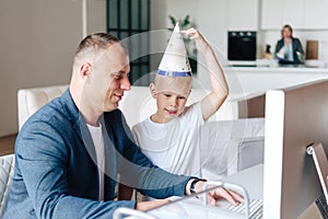 Happy father sits and works at the computer, next to him is a happy preschool child