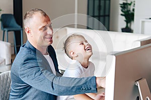 Happy father sits and works at the computer, next to him is a happy preschool child