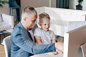 Happy father sits and works at the computer, next to him is a happy preschool child