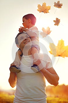 Happy father and son child walking together enjoying sunny autumn park, family on sunset, flying maple leaves