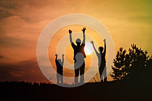 Happy father with son and daughter silhouettes play in sunset