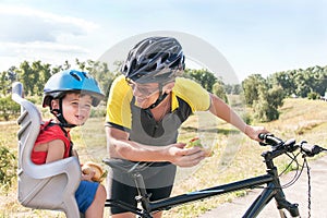 Happy father and son is eating lunch (snack) during bicycle ride