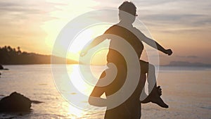 Happy father and son in eyeglasses playing on tropical beach boy rising up hands at stunning sunset with shining lens