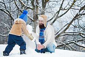 Happy father and son making snowman in the snow. Handmade funny snowman. Happy family plaing with a snowman on a snowy