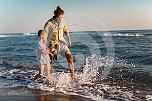 Father and son, man & boy child, running and having fun in the sand and waves of a sunny beach