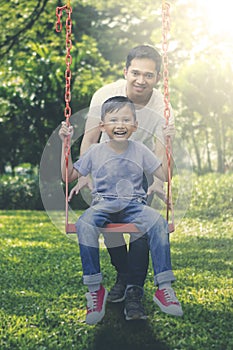 Happy father and son playing with a swing at park