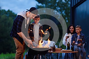 Happy father and son preparing a barbecue on a family vacation on the terrace of their modern house in the evening.