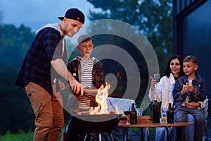 Happy father and son preparing a barbecue on a family vacation on the terrace of their modern house in the evening.