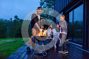 Happy father and son preparing a barbecue on a family vacation on the terrace of their modern house in the evening.