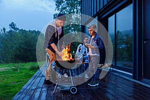 Happy father and son preparing a barbecue on a family vacation on the terrace of their modern house in the evening.