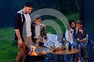 Happy father and son preparing a barbecue on a family vacation on the terrace of their modern house in the evening.